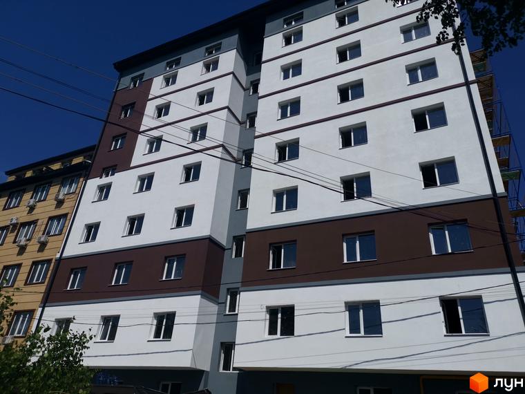 Новобудова Благовест з білим фасадом, коричневими та сірими смугами, численними вікнами. Поруч видно будівельні риштування та синє небо.