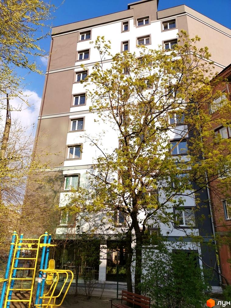 Висотна будівля з білими та коричневими фасадами. Поруч зелені дерева та дитячий майданчик. ЖК Захисник - ваш новий дім!