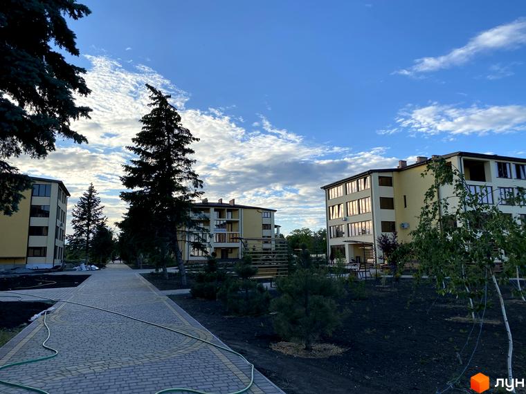 Житловий комплекс GRAND FAMILY APARTMENTS з жовтими фасадами та великими вікнами, оточений зеленими насадженнями та вимощеною алеєю.