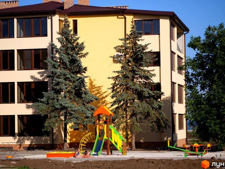 Житловий комплекс GRAND FAMILY APARTMENTS з дитячим майданчиком та зеленими насадженнями. Зовнішній вигляд будинку з вікнами та балконами.