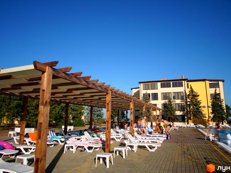 Будівля GRAND FAMILY APARTMENTS бежевого та жовтого кольорів. На прибудинковій території розташовані шезлонги під перголою та басейн.