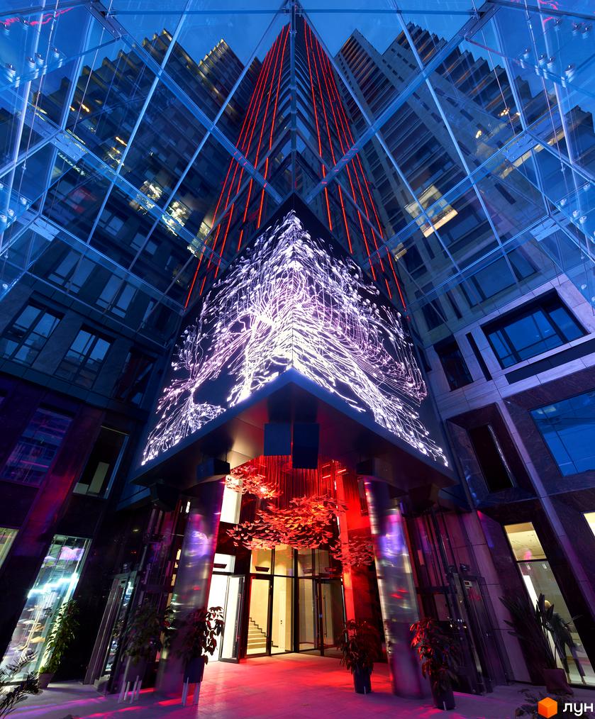 Фасад ЖК Chicago Central House з скляними панелями та неоновим підсвічуванням. Вхідна група з рослинами та декоративними елементами.
