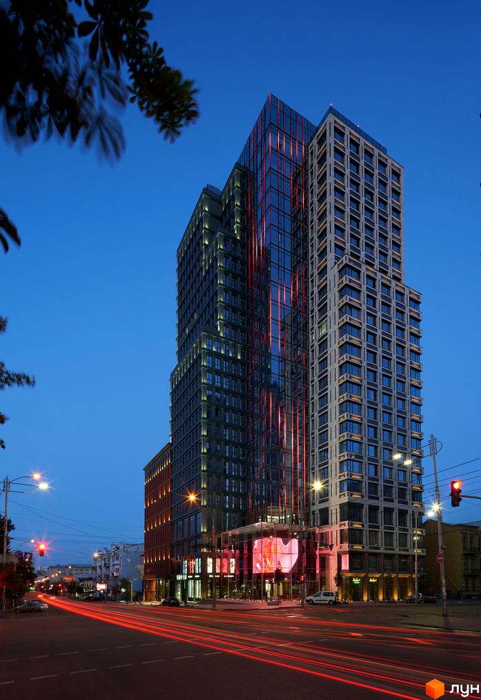 Висотна будівля ЖК Chicago Central House з скляним фасадом та підсвіткою. На передньому плані дорога з слідами від фар автомобілів.