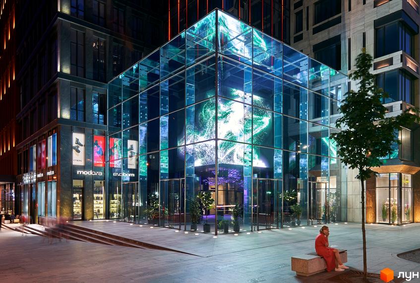 Житловий комплекс Chicago Central House. Велика скляна будівля з яскравою ілюмінацією вночі. Навколо будівлі розташована площа з лавками та деревами.