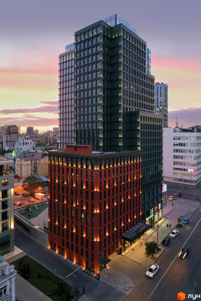 Житловий комплекс Chicago Central House. Висотна будівля з червоною цегляною основою та скляною надбудовою на тлі вечірнього неба. Біля будинку розташовані тротуари, дорога та припарковані автомобілі.