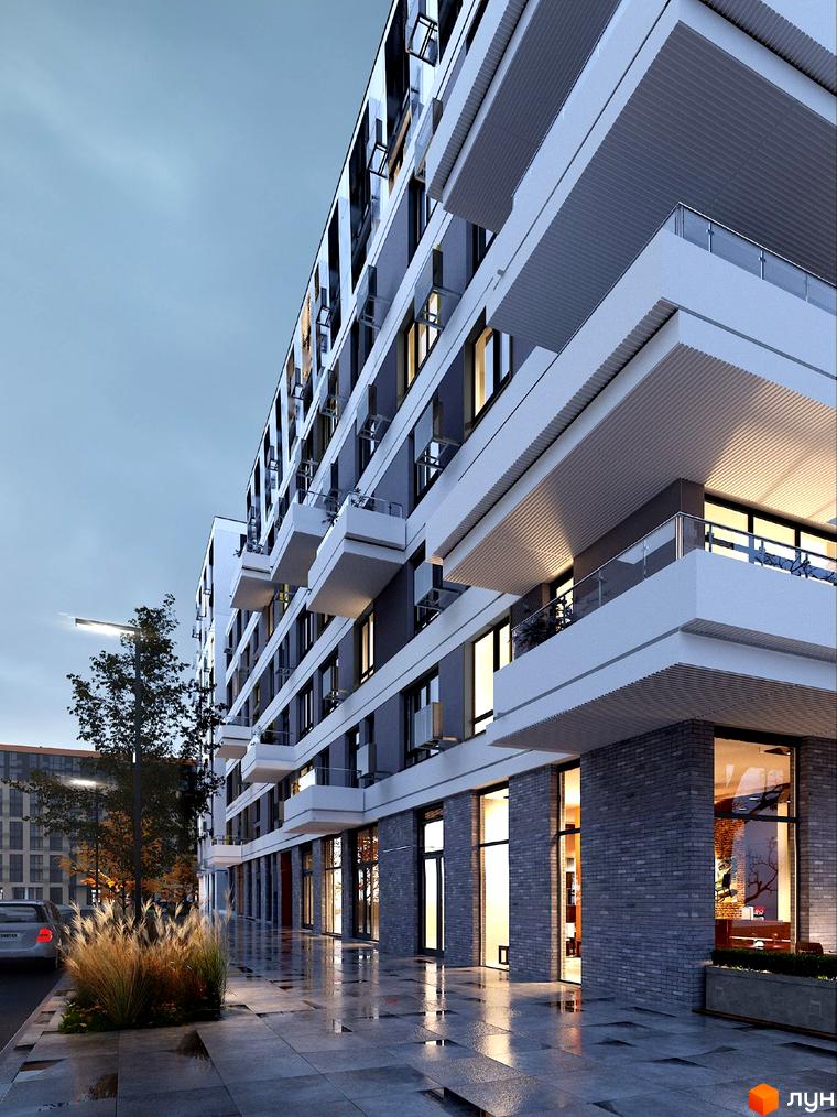 Багатоповерховий будинок з балконами та скляними перилами. На першому поверсі розташовані вітрини магазинів. На тротуарі видно відблиски від дощу.