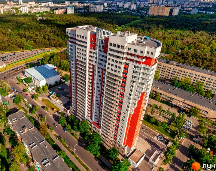 Багатоповерховий житловий будинок Житловий комплекс Воскресенський з біло-червоним фасадом, оточений зеленими насадженнями та міською забудовою.