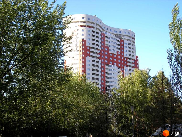 Житловий комплекс Воскресенський: високий будинок з хвилястим фасадом, білими та червоними секціями, оточений густими зеленими деревами під блакитним небом.