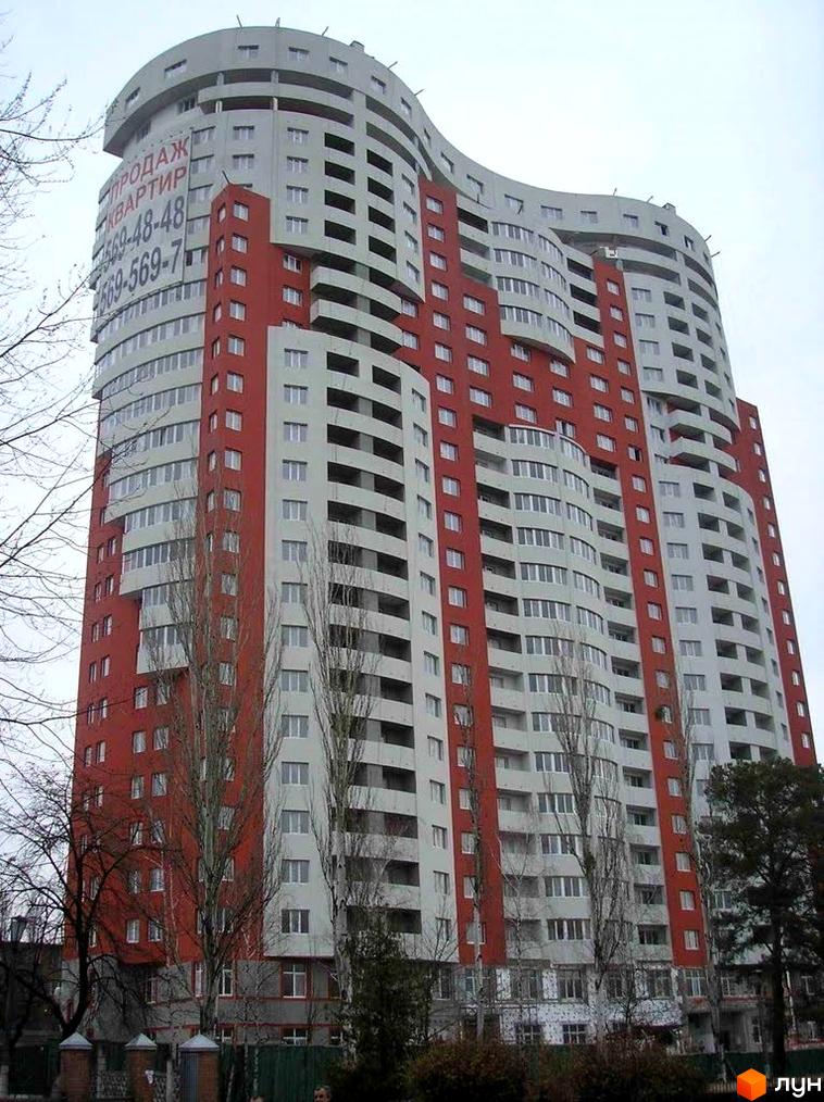 Багатоповерховий Житловий комплекс Воскресенський з хвилястим фасадом червоно-сірого кольору. На фасаді розміщено банер про продаж квартир, поруч видно дерева без листя.