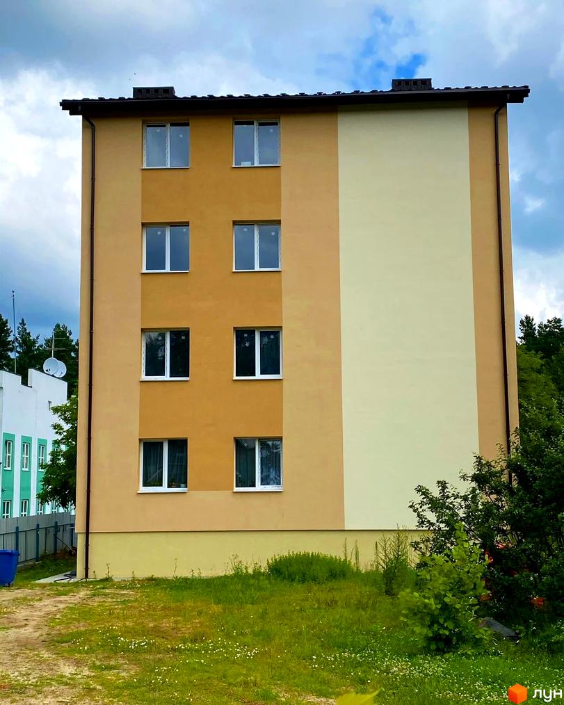 Зовнішній вигляд новобудови по вул. Спортова, 12 з вікнами та фасадом у два кольори. Навколо будинку зелена територія з травою та деревами.