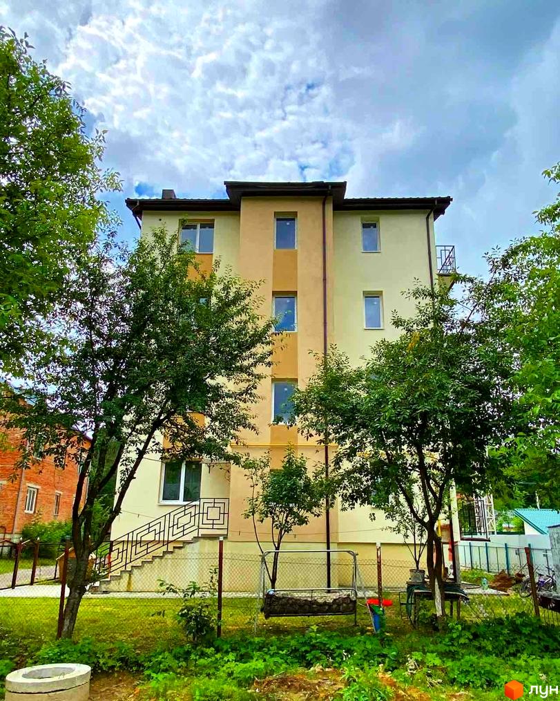 Фасад будинку на вул. Спортова, 12, з вікнами та балконами, оточений деревами та зеленою зоною.