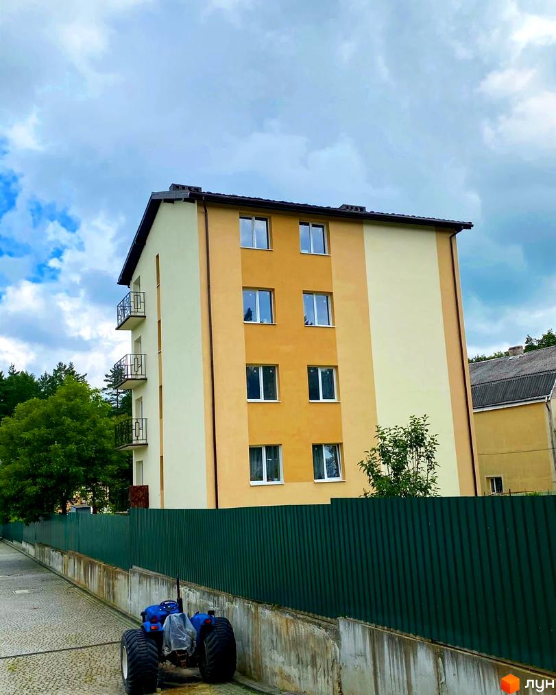 Новобудова на вулиці Спортова, 12, з фасадом у світлих тонах та балконами. Поруч зелений паркан та дорога з бруківки.