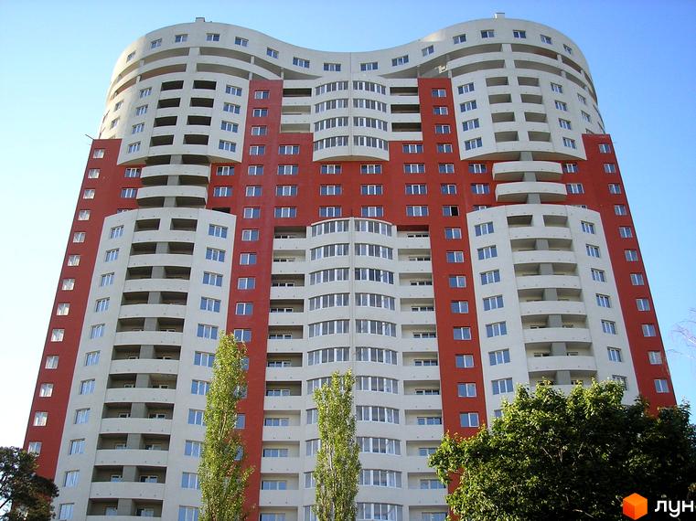 Багатоповерховий житловий комплекс Воскресенський з хвилястим фасадом червоного та світлого кольору. Навколо будинку видно зелені дерева.