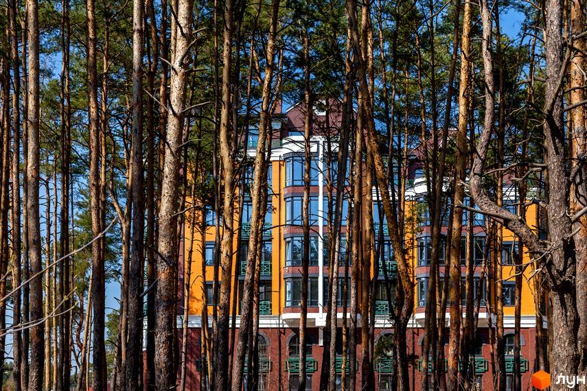 Клубний будинок „На Радистів“ з оранжевим фасадом та великими вікнами, оточений високими соснами. Фото новобудови.