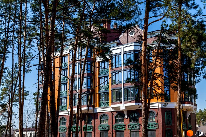 Клубний будинок „На Радистів“ з цегляним фасадом та великими вікнами, оточений високими соснами. Сучасна архітектура новобудови, що гармонійно вписується в природний ландшафт.