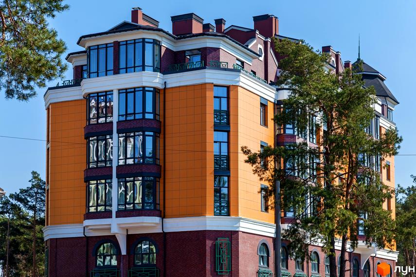 Клубний будинок „На Радистів“ з оранжевим фасадом та цегляною основою. Сучасна архітектура новобудови з великими вікнами та елементами декору.