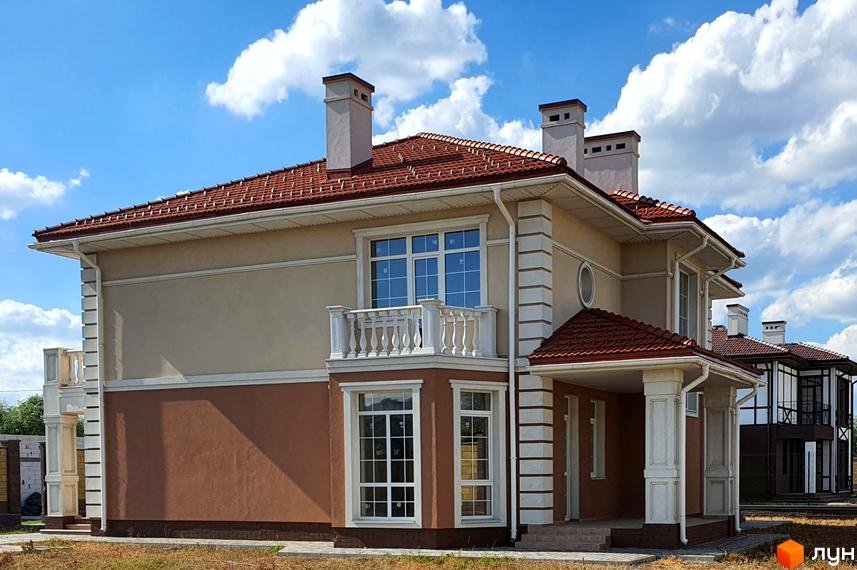 Зображення будинку в Котеджному містечку Осокор. Двоповерховий будинок з коричневим дахом та світлим фасадом, балкон з білими перилами.