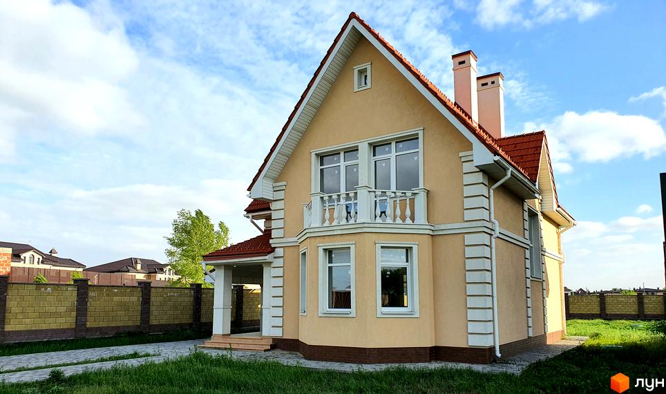 Зображення будинку в Котеджному містечку Осокор. Двоповерховий будинок з балконом та червоним дахом, зелена прибудинкова територія.