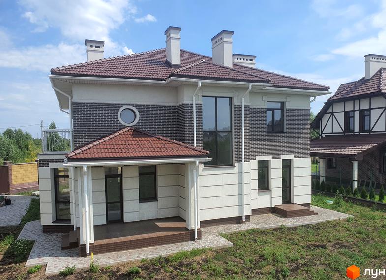 Двоповерховий будинок з коричневою черепичною покрівлею та цегляною кладкою. Перед будинком розташована вимощена доріжка та зелена трава.