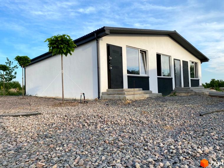 Таунхаус Белгород – одноповерхова біла будівля з темним дахом та дверима, розташована на ділянці, засипаній сірим щебенем.