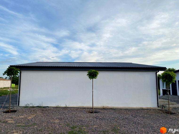 Білий фасад таунхауса Комплексу таунхаусів „Белгород“ з темним дахом та водостічною системою. На гравійній прибудинковій території висаджені молоді дерева.