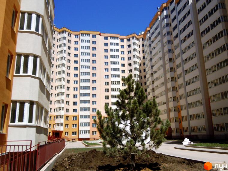 Житловий комплекс Райдужний з фасадом з великими вікнами та прибудинковою територією з зеленими насадженнями.