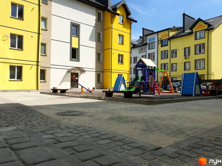 Житловий комплекс Мілан: яскрава фасадна частина будівель та дитячий майданчик з гірками та гойдалками. Територія комплексу впорядкована бруківкою та лавками.