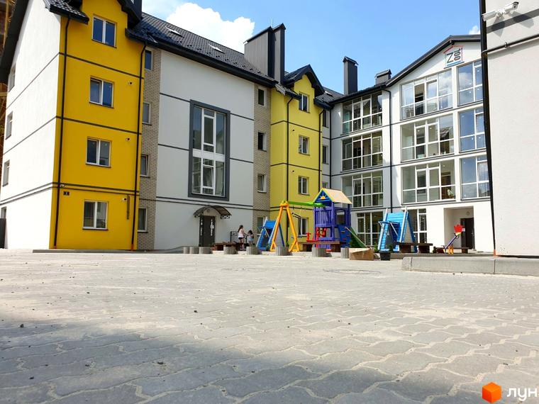 Житловий комплекс Мілан: жовтий та білий фасади будівель з великими вікнами. Дитячий майданчик з гірками та гойдалками на прибудинковій території.