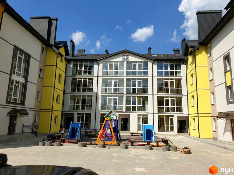 Зовнішній вигляд житлового комплексу Мілан з жовтими та білими фасадами, великими вікнами та дитячим майданчиком на прибудинковій території. Новобудова з сучасною архітектурою.