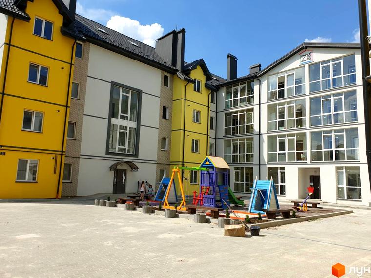 Зовнішній вигляд новобудови ЖК Мілан з жовтими та білими фасадами. На прибудинковій території розташований дитячий майданчик з гірками та гойдалками.