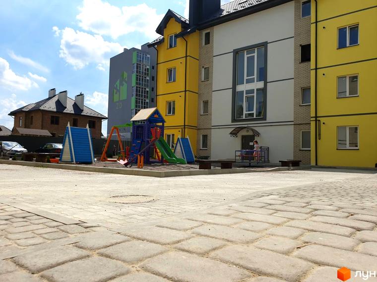Житловий комплекс Мілан. Зовнішній вигляд жовтих та білих будинків з дитячим майданчиком та зеленими насадженнями.