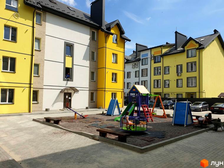 Житловий комплекс Мілан: фасади жовтих та білих будинків, дитячий майданчик з гірками та гойдалками, зони відпочинку.