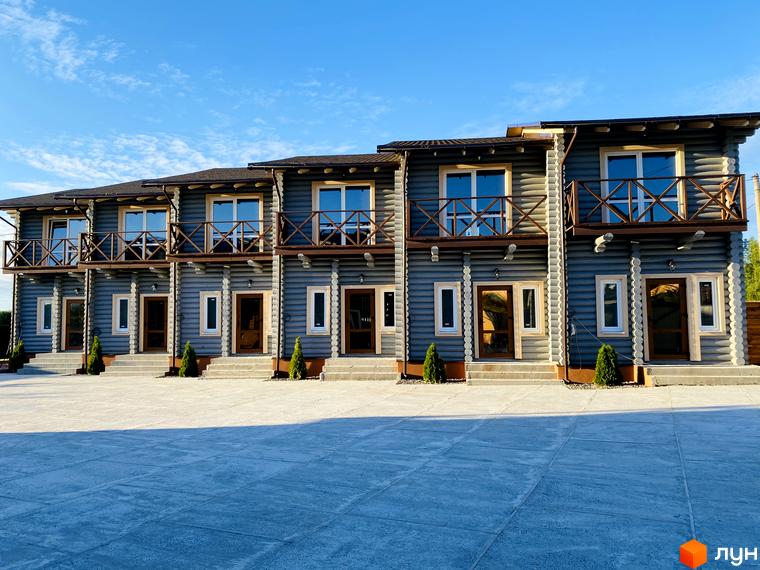 Зовнішній вигляд таунхаусів LEVEL, побудованих з дерева, з балконами та великими вікнами. Перед будинками розташований вимощений двір.