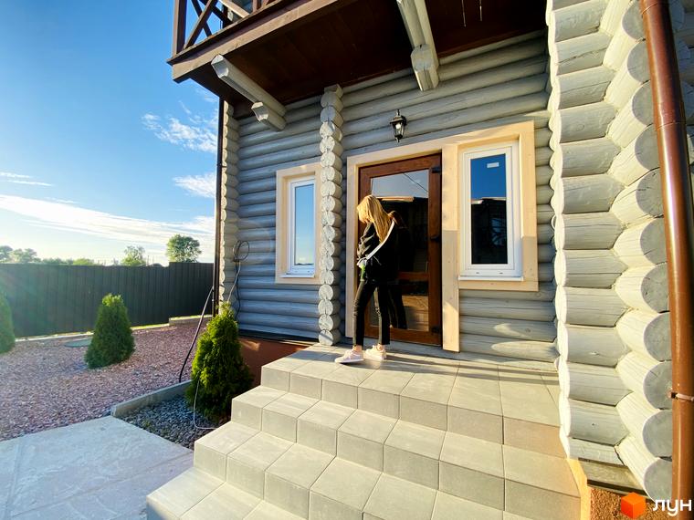 Таунхаус „LEVEL“: будинок зі світлого дерев'яного зрубу з балконом, сірі сходи та доріжка з гравію. Прибудинкова територія озеленена туями.