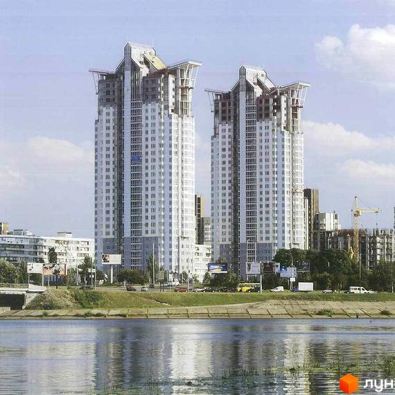 Дві висотні будівлі Житлового комплексу Silver Breeze з світлими фасадами та складними даховими конструкціями. Розташовані біля річки з дорогою та забудовою.