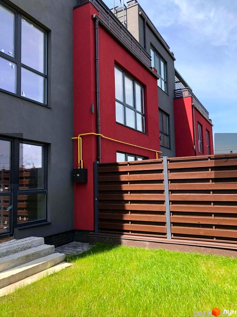 Таунхауси Old Stories з червоно-сірим фасадом та дерев'яним парканом. Зелена галявина перед будинком.