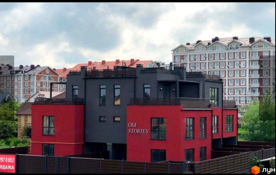 Таунхауси Old Stories – це сучасні двоповерхові будинки з червоною та сірою обробкою, розташовані біля високої новобудови.