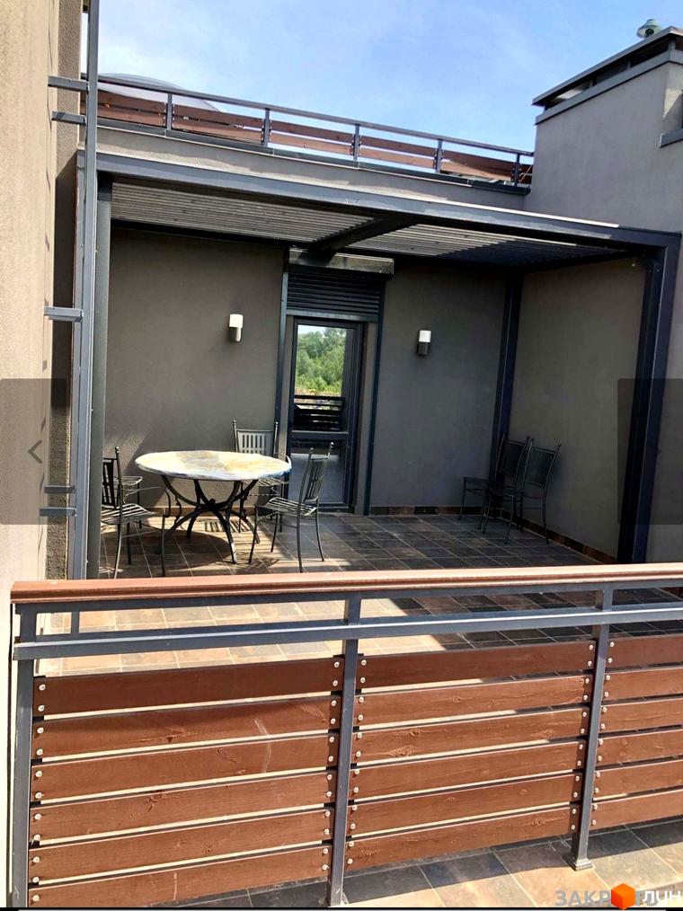 Таунхауси Old Stories: затишна тераса з меблями та дерев'яним огородженням на тлі будинку під блакитним небом. Ознайомтеся з плануваннями та цінами.