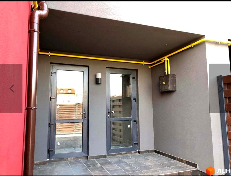 Зовнішній вигляд таунхаусів Old Stories з дверима та вікнами, що виходять на терасу з газовою трубою. Територія біля будинку з бруківкою та парканом.