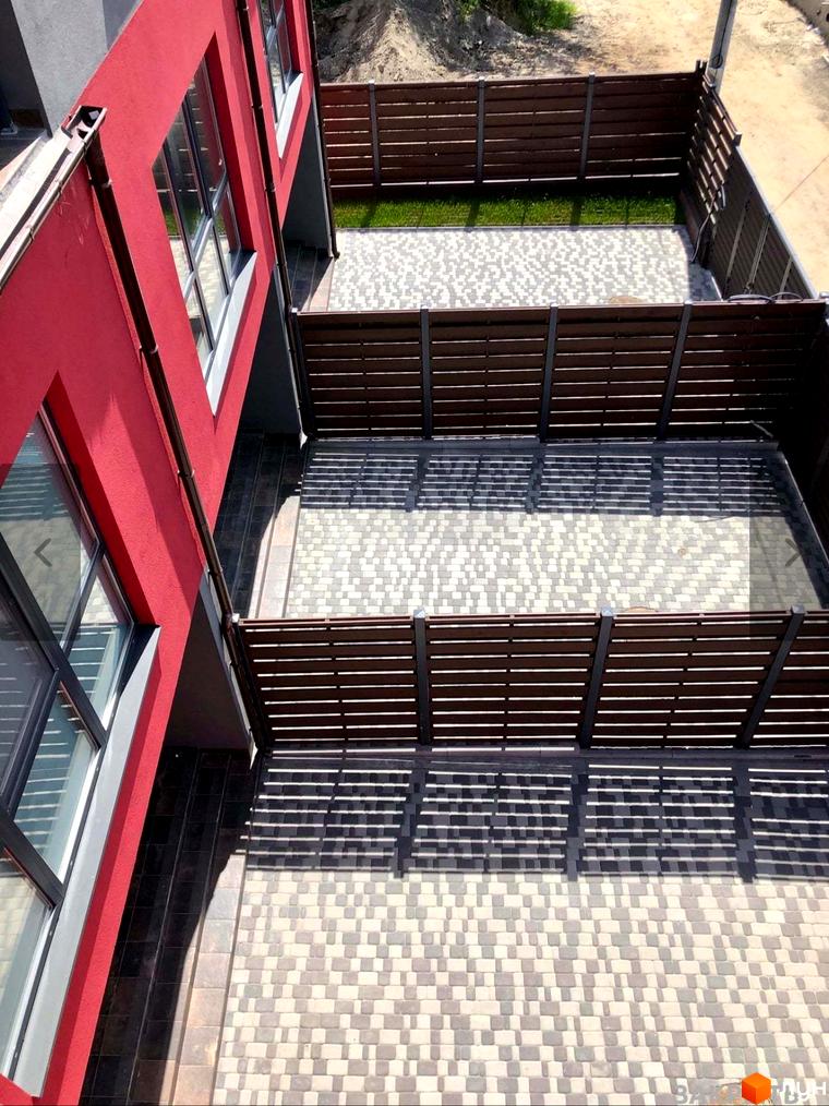 Зовнішній вигляд червоного таунхаусу Old Stories з вікнами та дерев'яною огорожею прибудинкової території з бруківкою.