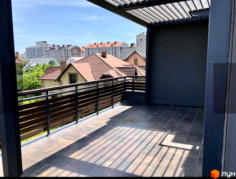 Вид з тераси на таунхауси Old Stories з коричневими дахами та зеленими деревами. На терасі плитка та дерев'яні перила.