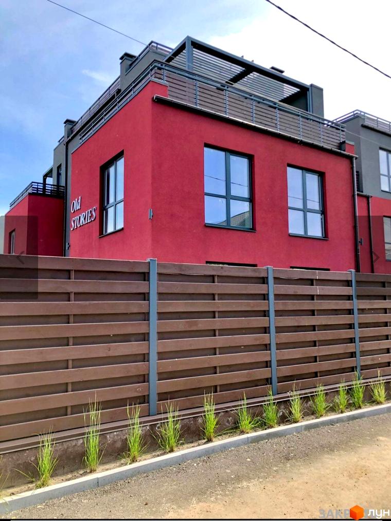 Таунхауси Old Stories з червоним фасадом та дерев'яним парканом. Навколо новобудови облаштована прибудинкова територія з зеленню.