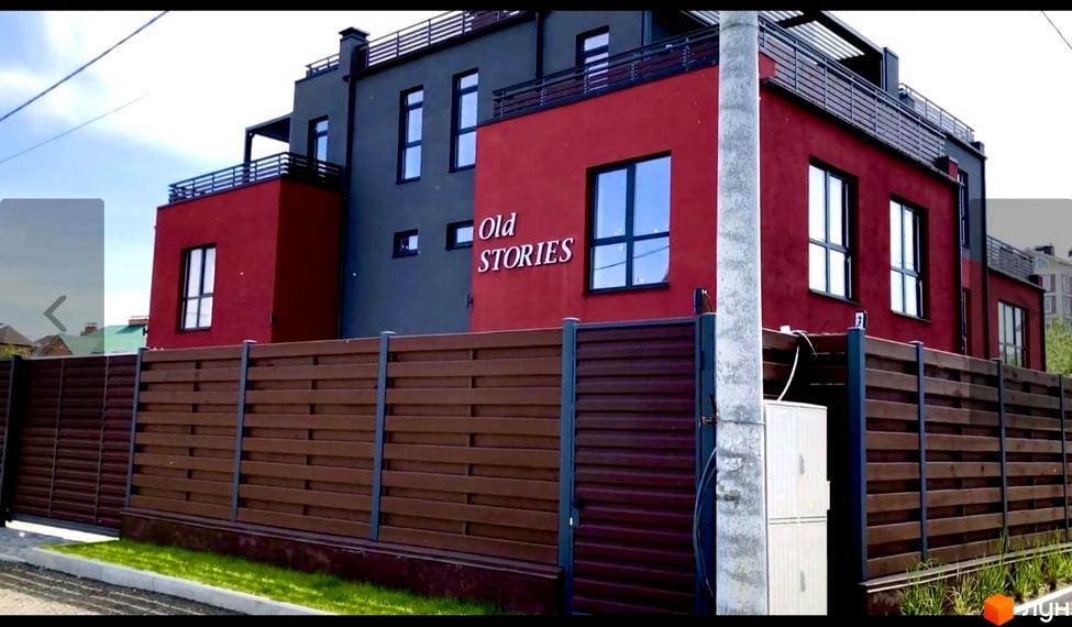 Таунхауси Old Stories у червоно-сірому кольорі з коричневим парканом та зеленою зоною. Зовнішній вигляд будинку та прибудинкова територія.