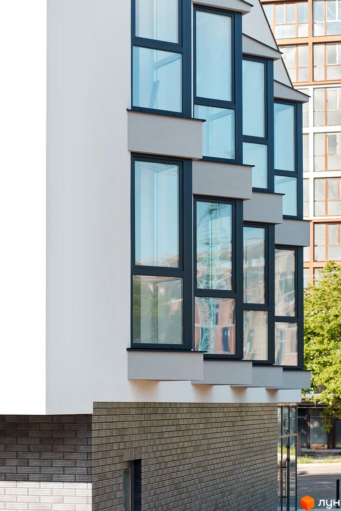 Клубний будинок Craft з великими вікнами та сірою цегляною кладкою фасаду. Навколо будинку зелені дерева та сусідні будівлі.