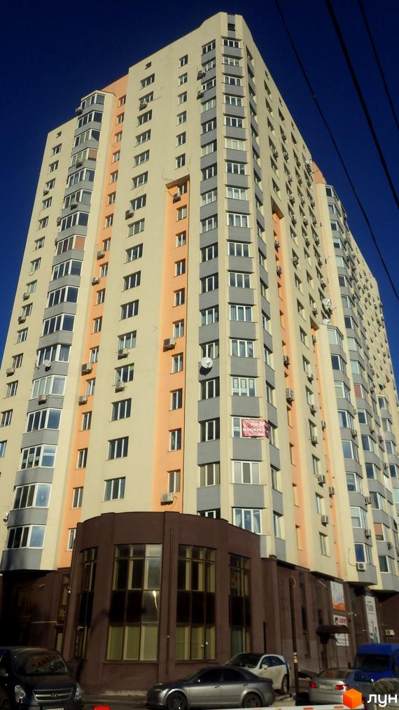 Житловий комплекс на вул. Борщагівська, 208, з сучасним фасадом та прибудинковою територією, де паркуються автомобілі.