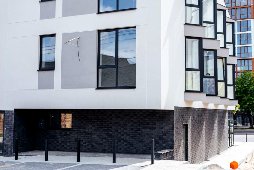 Зовнішній вигляд клубного будинку Craft з великими вікнами та цегляною обробкою цоколя. Навколо будинку облаштована прибудинкова територія з паркувальними місцями та стовпчиками.