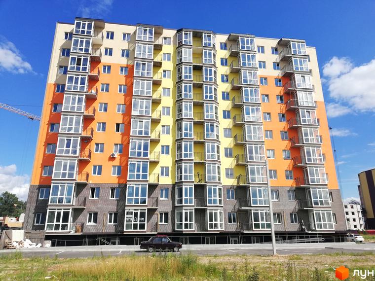 Яскравий багатоповерховий будинок ЖК Європейський Двір з балконами та великими вікнами. На передньому плані - парковка та зелена трава.