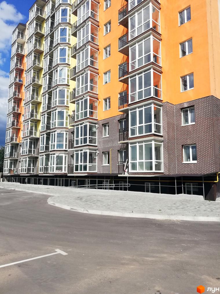 Висотна будівля житлового комплексу Європейський Двір з панорамними вікнами та балконами. Поруч асфальтована дорога та тротуар з бруківкою.