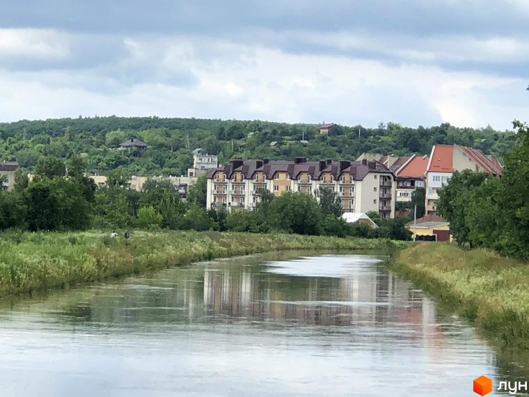 Житловий комплекс Котляревського. Багатоквартирні будинки з коричневими дахами та світлими фасадами розташовані біля річки на тлі зелених пагорбів.