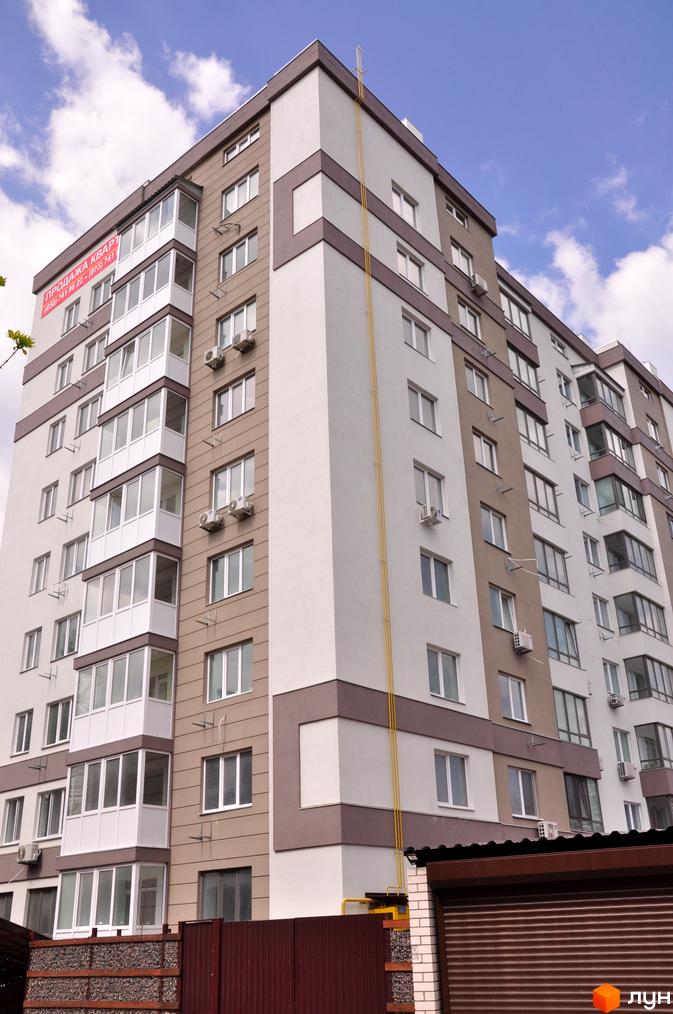 Зовнішній вигляд багатоповерхового будинку житлового комплексу Мирний з балконами та кондиціонерами. На фасаді є реклама про продаж квартир.